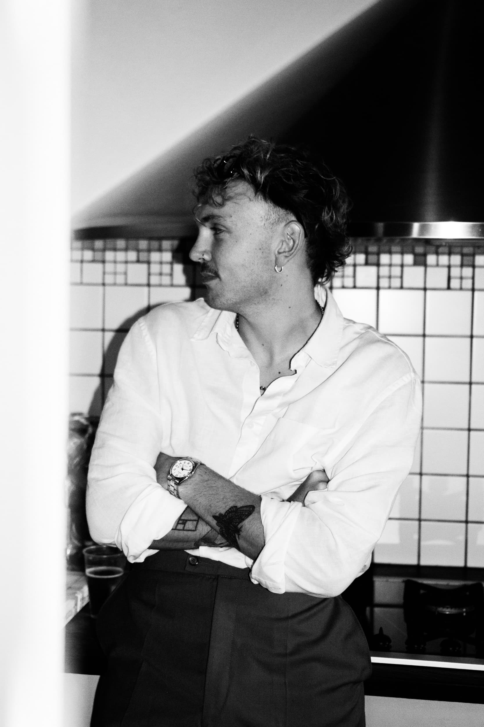 A member of the collective in a white shirt, arms crossed, in a tiled kitchen