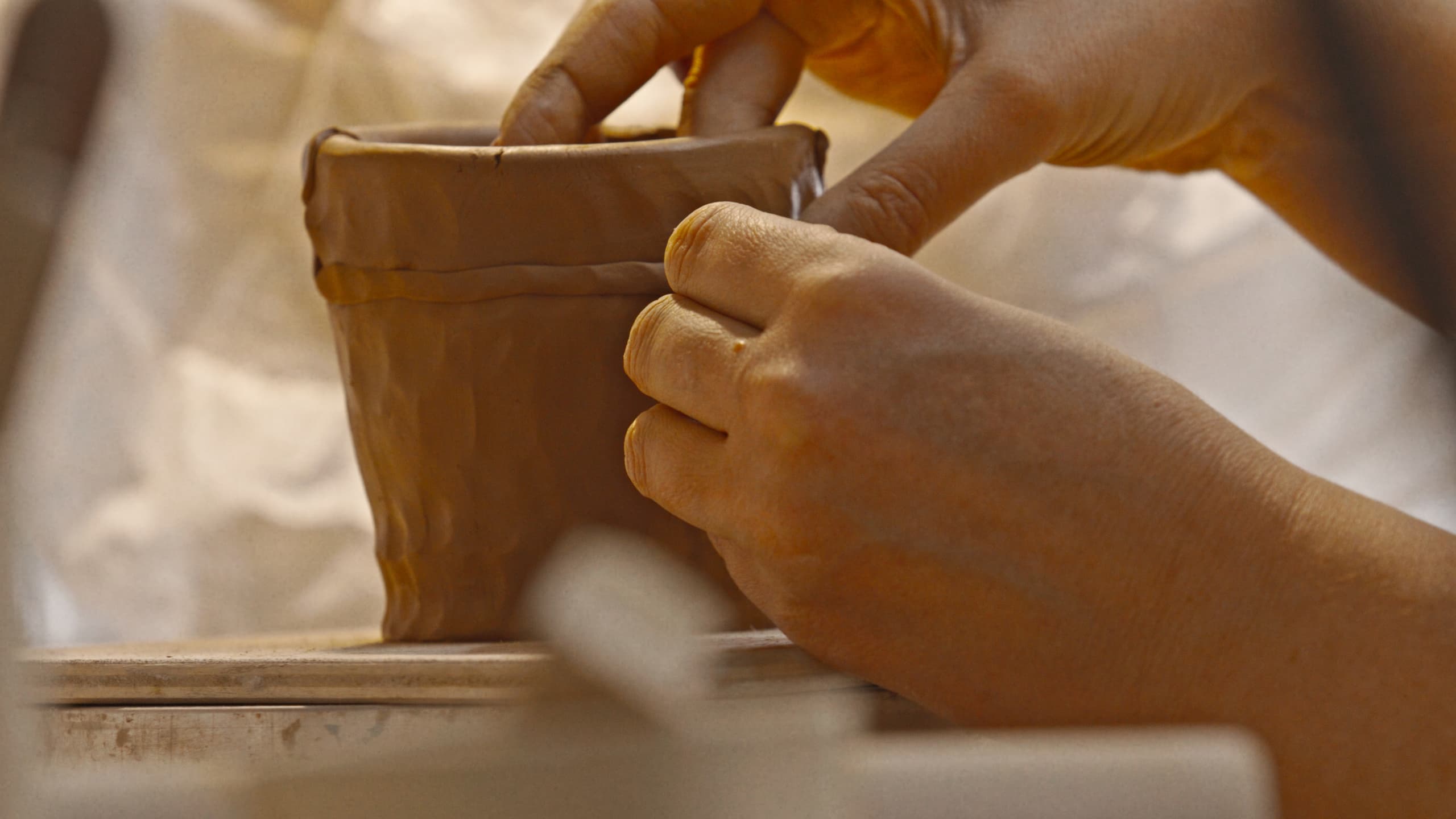 Hands forming the wall of a clay pot