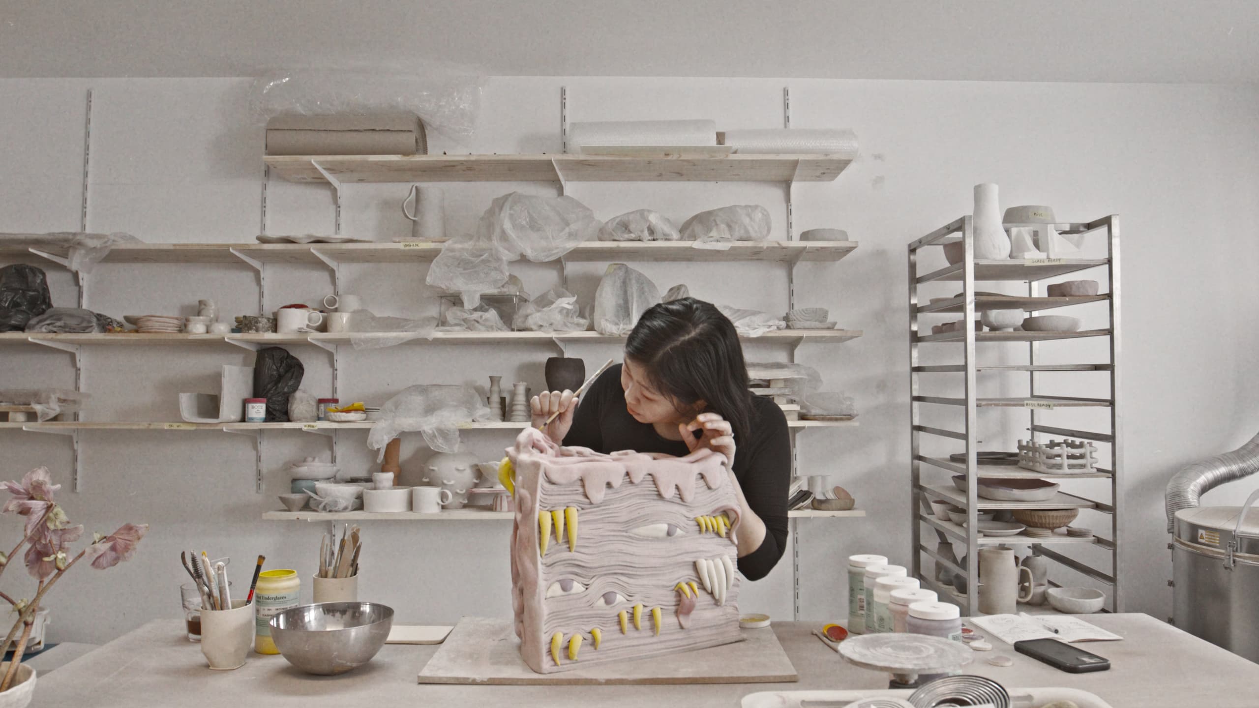 The studio, shelves of ceramics behind the bench