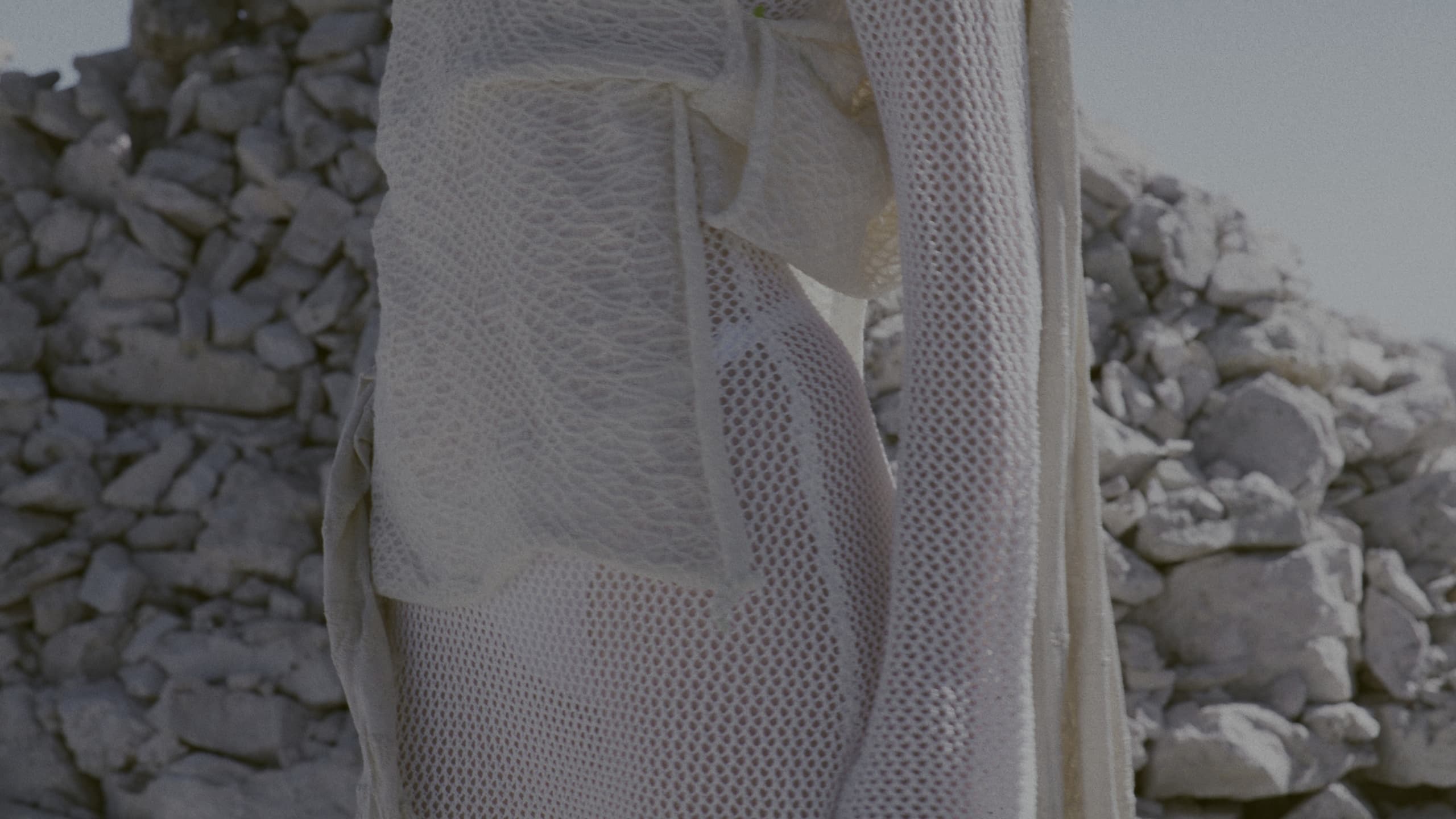 Open-knit Pecoranera garment against stacked stone